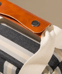 Close-up of a bag with a brown leather handle and striped fabric.