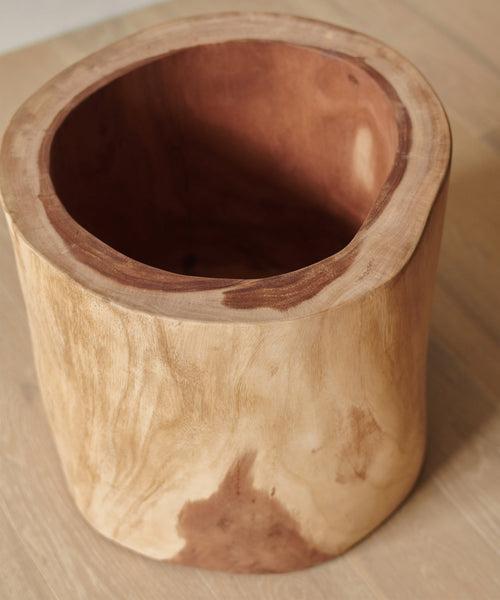 The Ranch Planter features smooth, cylindrical Suar wood with natural grain patterns and a hollowed interior. Ideal as a rustic indoor planter, it sits beautifully on any light wooden surface.