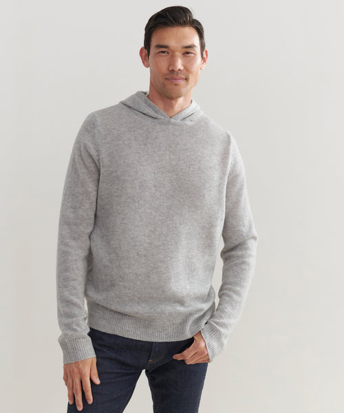 A man stands against a plain background, wearing the Mens Hoodie in light gray and dark blue jeans, with one hand in his pocket and a slight smile on his face.