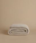 A folded knit blanket in a light oatmeal beige color, displayed on a matching solid beige background.