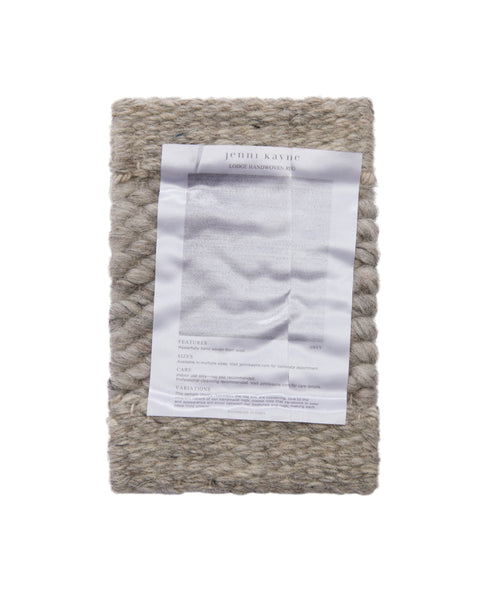 A rectangular Rug Swatch in chunky light gray woven fabric is shown with a paper label featuring text and an image of the same sample, all set against a white background.
