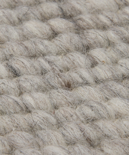Close-up of the Rug Swatch displays thick, chunky light gray and beige fibers in a woven texture. Visible loops and strands give this swatch a soft, natural lodge-style appearance.