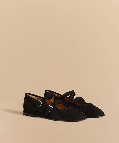 The Wren Flat, black suede Mary Jane shoes with a rounded square toe, double straps, and silver buckles, are displayed on a plain beige background.