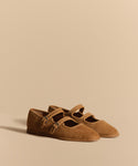 The Wren Flat is a tan suede Mary Jane with double straps, small buckles, and a rounded square toe, shown against a matching beige background.