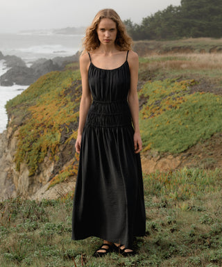 Woman in a black wynn dress standing on a grassy hill with ocean view