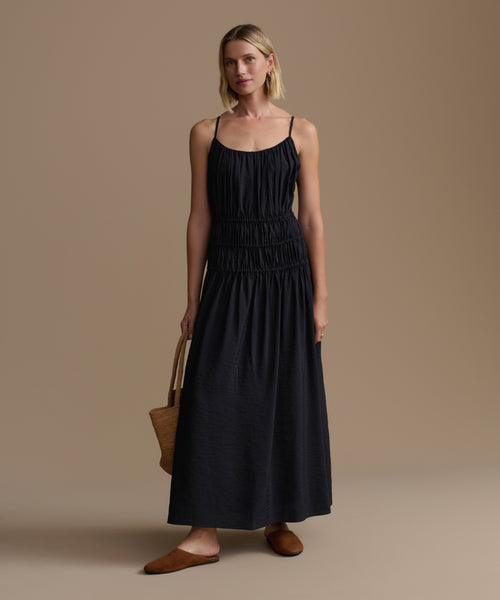 Woman wearing a black wynn dress holding a brown bag against a beige background