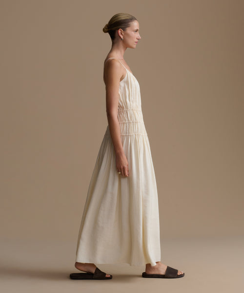 Woman wearing a long, cream wynn dress against a plain background