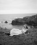 Woman in a cream wynn dress lying on grass by the ocean