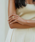 A woman in a sleeveless cream ribbed dress crosses her arms, showcasing the Campbell Cigar Band ring on her left hand. Her dark, wavy hair frames her upper body against a light background.