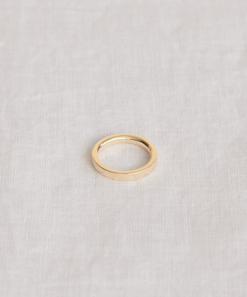 The James Band, a simple 14k solid gold ring, rests on a light textured fabric, reflecting the timeless elegance of heirloom-quality jewelry.