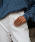 A person in a chunky blue knit sweater and white pants rests their left hand, wearing the James Band from Jenni Kayne Jewelry, in their pocket.