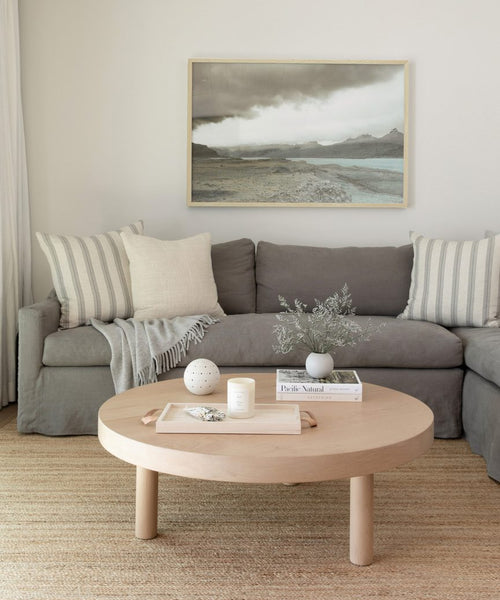 A cozy living room with a grey sofa, striped and plain pillows, a light throw blanket, a round wooden coffee table with decor, and the Awash 5 Framed Print displayed on the wall above the sofa.