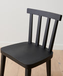 A Hampton Dining Chair in black oak with a slatted backrest sits on a light wood floor against a plain white wall.