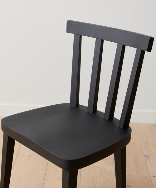 A Hampton Dining Chair in black oak with a slatted backrest sits on a light wood floor against a plain white wall.