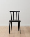 A Hampton Dining Chair in black oak with a slatted backrest sits on a light wood floor against a plain white wall.