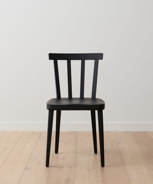 A Hampton Dining Chair in black oak with a slatted backrest sits on a light wood floor against a plain white wall.