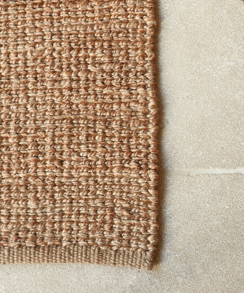 A close-up of the Bramble Rug’s thick, natural jute fibers highlights its handmade texture, creating a striking contrast with the smooth, light stone or tile floor beneath.
