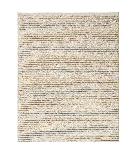 A close-up of the Palermo Rug’s corner shows its beige, textured linen wool surface with horizontal ridges. This sustainable rug feels soft underfoot and features a simple, minimalist design.