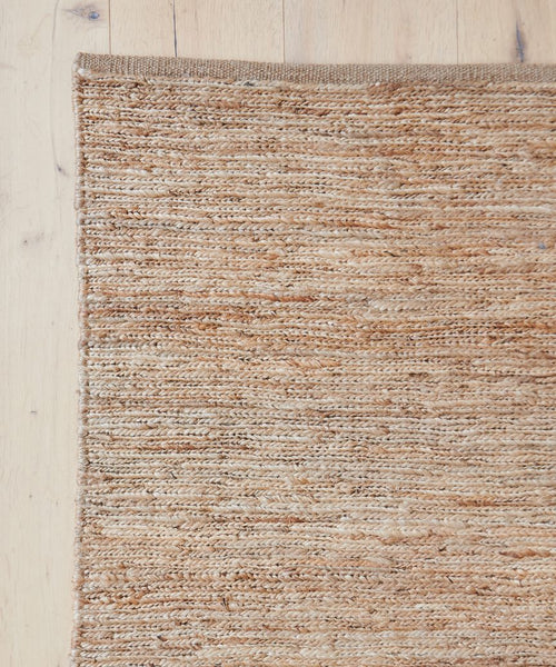 A close-up of the River Rug, a handwoven flatweave, placed on a light wood floor, highlighting its rich texture and sustainable natural fibers.