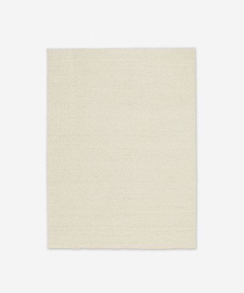 The Dune Rug, a rectangular off-white hand-knotted wool piece with a simple, solid color design, is displayed on a light gray background.