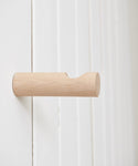 The Oak Wall Hook features a minimalist handmade rounded design in rustic white oak, shown mounted on a white wall with vertical paneling.