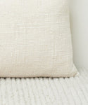 The Luna Lumbar Pillow, handwoven with a feather down insert, rests on a soft white carpet.