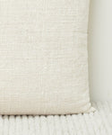A close-up of the Luna Pillow, showcasing its textured, handwoven ivory design as it rests against a matching ribbed surface with a soft, woven look.
