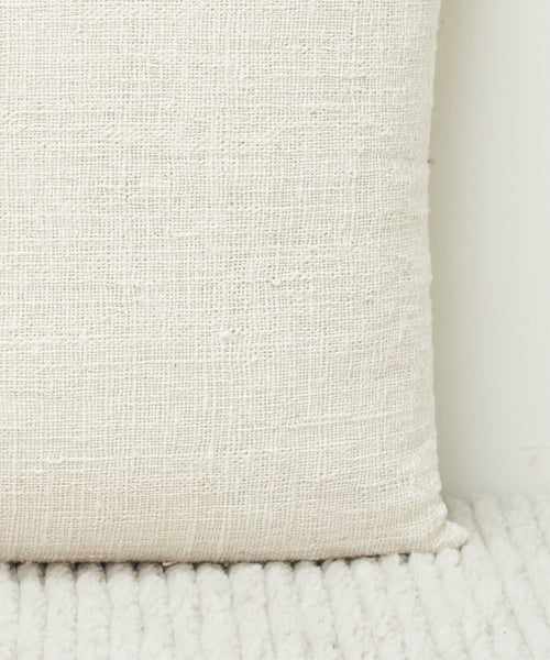 A close-up of the Luna Pillow, showcasing its textured, handwoven ivory design as it rests against a matching ribbed surface with a soft, woven look.