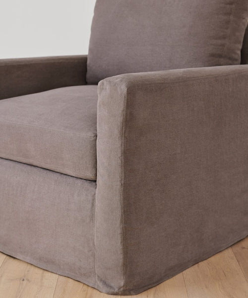 A close-up of the Harbor Chair, a modern gray upholstered armchair with a boxy design, sits on a light wooden floor against a white wall. The chair is handmade in Los Angeles, showcasing local craftsmanship.