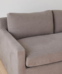 A close-up of the Harbor Sofa, handmade in Los Angeles with modern light gray fabric, clean lines, and two back cushions, shown against a white wall on a light wood floor.