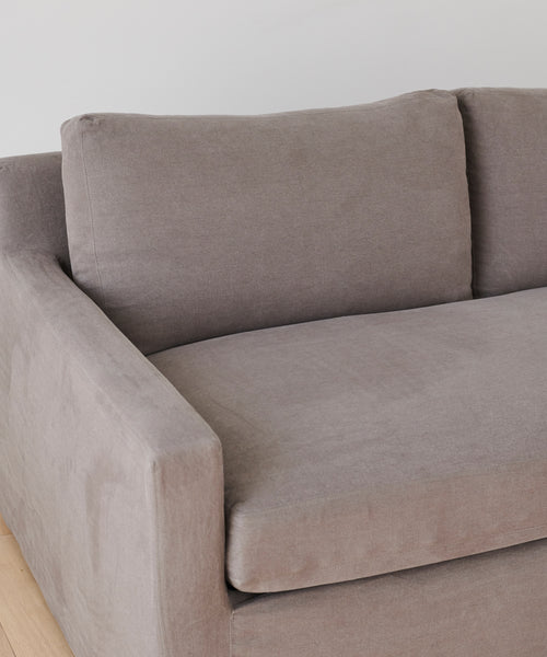 A close-up of the Harbor Sofa, handmade in Los Angeles with modern light gray fabric, clean lines, and two back cushions, shown against a white wall on a light wood floor.