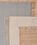 Three rectangular woven rugs are layered: a gray rug on the left, a beige handwoven rug in the center, and the Hudson Jute Rug with coarse texture underneath.