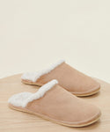 The Lodge Outdoor Slipper features a tan suede upper and white shearling lining, shown on a light wooden surface against a neutral background.