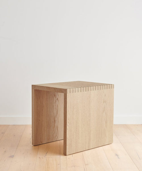 The Malibu Side Table, featuring clean lines and visible dovetail joints, stands on a light wood floor against a plain white wall, showcasing its minimalist design.