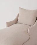 The Miramar Chaise Slipcover, in beige Belgian linen, covers an upholstered chaise lounge with a matching back cushion, styled against a plain white wall for a minimalistic look.