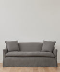 The Miramar Sofa, in simple gray Belgian linen with feather down fill and two matching pillows, sits against a plain white wall on a light wooden floor.
