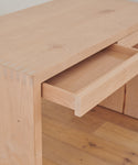 A close-up of the Newport Desk with one drawer partially open, highlighting its light wood grain and dovetail joints, set on a wooden floor.