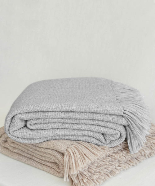 Two folded Large Alpaca Basketweave Throws, one light gray and one beige, are handwoven in Peru from super-soft alpaca. Both display a textured look with fringed edges and are stacked against a plain, light background.