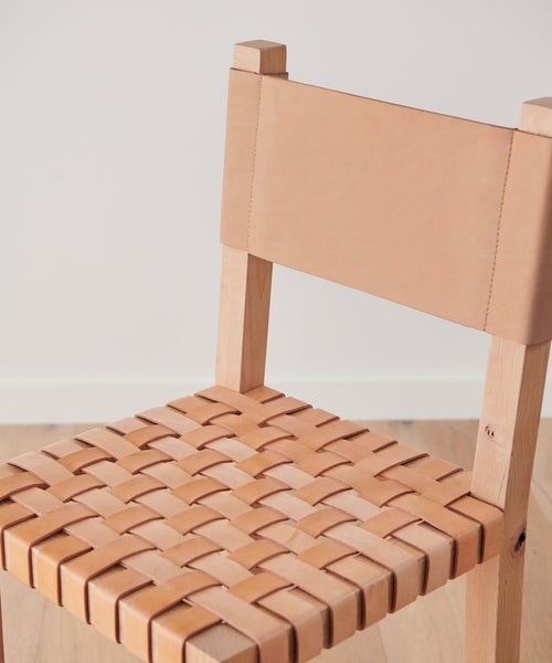 A close-up of the Tahoe Counter Stool shows its woven leather seat and solid leather backrest. The Knotty Alder wood frame contrasts against a plain white wall, while the stool stands on a light wood floor.