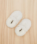 A pair of Shearling Baby Booties in fluffy white, featuring closed toes, sits side by side on a light wooden floor.