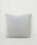 The Sonoma Pillow in light gray stands upright on a textured cream surface, set against a white vertical paneled wall.