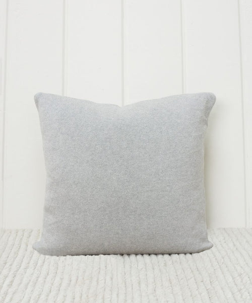 The Sonoma Pillow in light gray stands upright on a textured cream surface, set against a white vertical paneled wall.