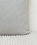 A close-up of the Sonoma Pillow in light gray fabric rests on a white textured surface, with a plain white wall in the background.
