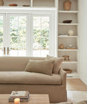 The Miramar Sofa sits in a room with shelves and windows, bringing comfort and elegance to the inviting space.