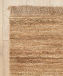 A close-up of the Mojave Jute Rug, handmade in India with horizontal ridges and fringed edges, shown on a light wooden floor.
