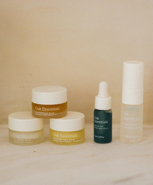 Five Oak Essentials’ Mini Routine features creams in glass jars, an oil with a dropper, and a pump—beautifully displayed on a light surface with a neutral background—making it the perfect travel companion.