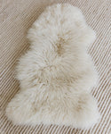 The Arctic Sheepskin rug, soft and ivory, is placed atop a ribbed, textured beige carpet.
