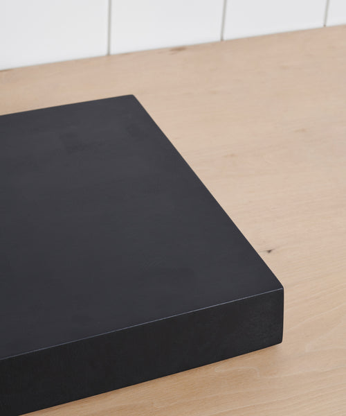 A Square Butcher Block sits on a light wooden countertop, backed by a white tiled wall.