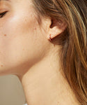 Close-up of a person’s face with smooth skin, freckles, light brown hair, and wearing the Huggie—a small rose gold hoop earring. Soft lighting highlights natural texture and the minimalist style of the jewelry.