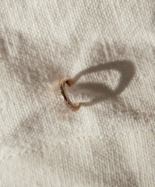 The Huggie with Diamonds, a small 14K gold earring set with diamonds, rests on textured off-white fabric and casts a delicate curved shadow.